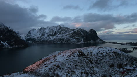 stunning drone flight over reine, lofoten islands, norway, featuring snowy mountains, the ocean, and a cloudy sky
