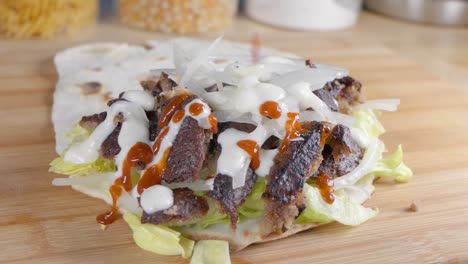 Zeitlupen-Slider-Aufnahme-Von-Spritzender-Scharfer-Soße-Auf-Einem-Döner-Kebab-In-Naan-Brot-Zu-Hause-In-Der-Küche