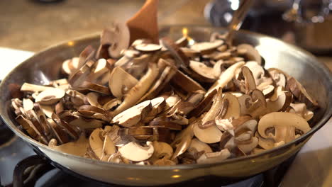 chef stirs raw sliced mushrooms in hot frying pan with wooden spoon