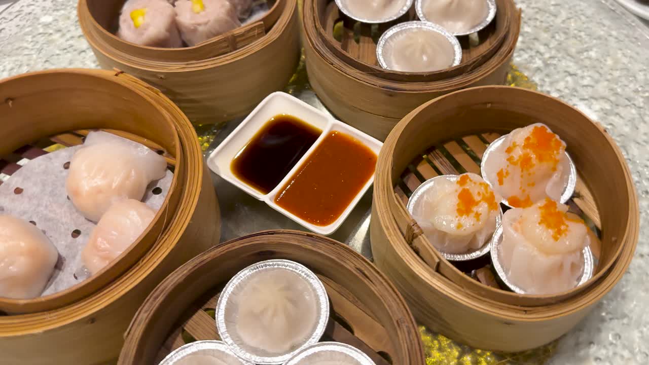 A vibrant spread of dim sum with dumplings, sauces, and bamboo baskets on a table. Bright lighting enhances the appetizing display