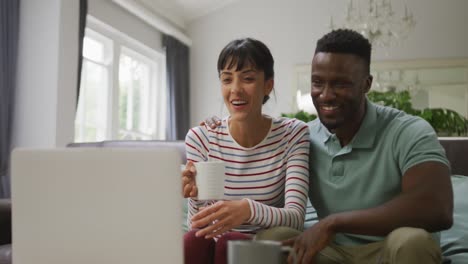 Happy-diverse-couple-sitting-on-couch-and-using-laptop-in-living-room