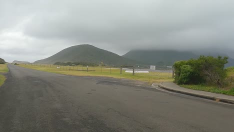 conduciendo a lo largo de lagoon rd lord howe island pasando por el aeropuerto local en un día lluvioso y nublado
