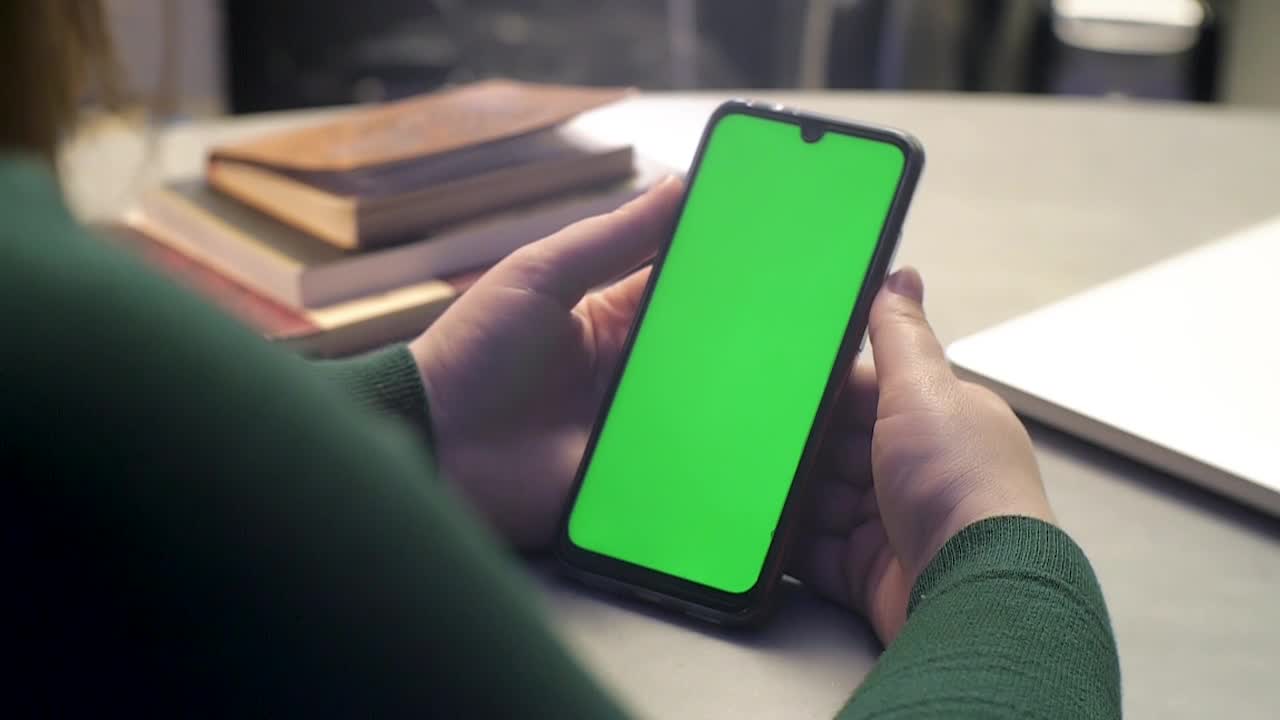 Ragazza che tiene uno smartphone tra le mani e lo usa. Il telefono, con schermo verde (chroma key) Android, mostra il display mentre lei tocca, scorre le funzioni, accende e spegne il dispositivo.