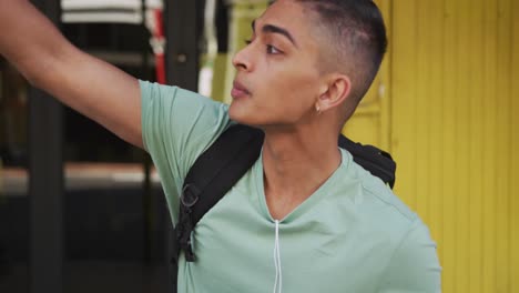 Mixed-race-man-holding-coffee,-rising-his-hand-up-in-the-street