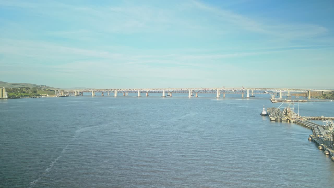 Drone tracking left of bridges connecting Carquinez Strait shoreline and wetlands, surrounded by hills in Martinez, California