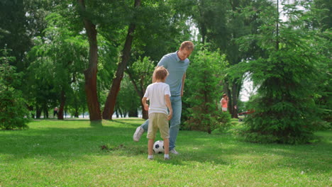 happy father teaching son play soccer. cheerful boy passing ball to dad on lawn.