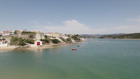 Aerial-view-away-from-a-anchored-boat-at-the-Mira-river-in-Vila-Nova-de-Milfontes,-sunny-Portugal---pull-back,-drone-shot