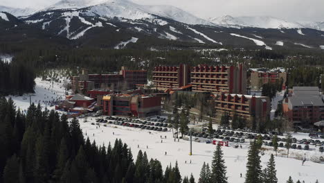 Rising-drone-footage-of-the-Beaver-Run-Resort-and-Conference-Center,-Breckenridge-mountain-range-,-and-a-ski-lift-with-skiers-and-snowboarders-in-Breckenridge,-Summit-County,-Colorado