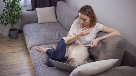 blonde woman sitting on a sofa, pays for purchases online with a credit card and laptop