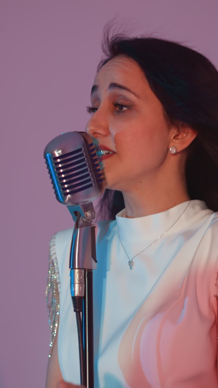 색 드레스를 입은 여성 가수가 빈티지 마이크 앞에 서서 손을 표현적으로 움직여 열정적으로 노래하고 있습니다. 기타리스트가 배경에서 연주합니다.