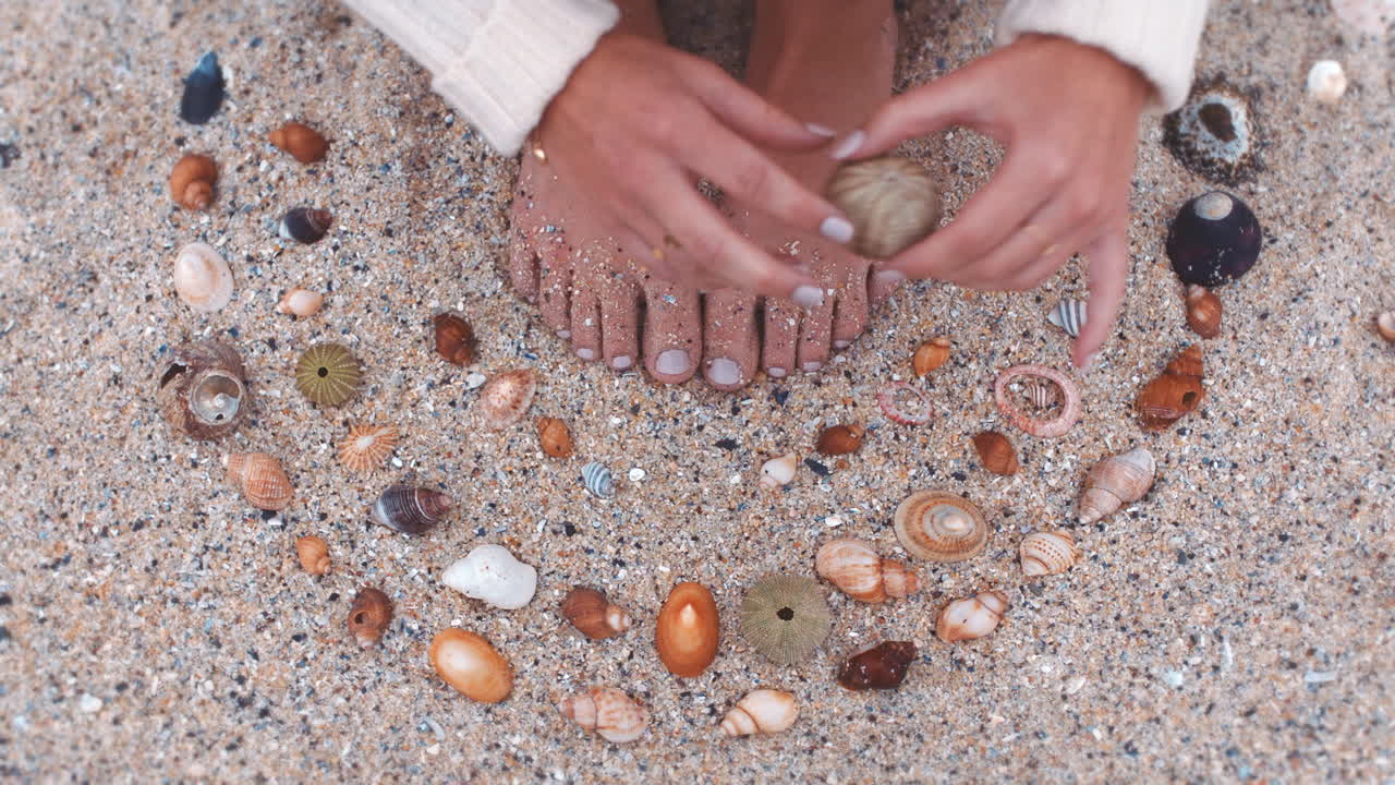 pies de la mujer, concha y arena de la playa mientras está sentado
