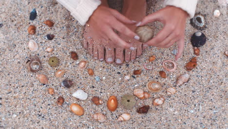 Frauenfüße,-Muschel-Und-Strandsand-Im-Sitzen