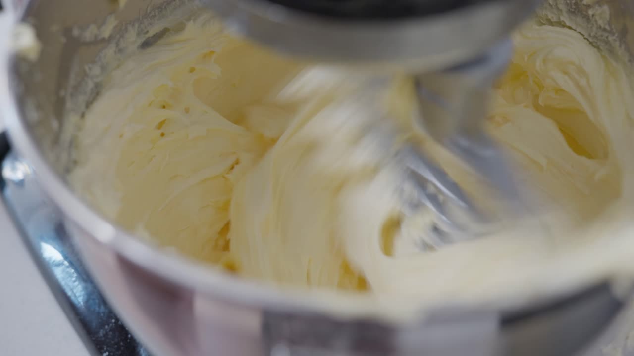 A Stand mixer whipping vanilla buttercream with the paddle attachment, as it turns and blends together making it creamy and smooth