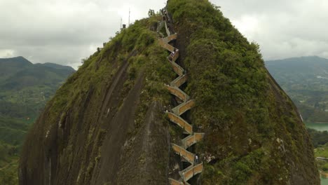 People-Climbing-Up-Steps-to-Top-of-Guatape-Rock,-Drone-View