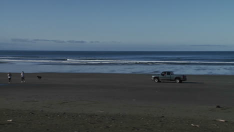 a truck drives across a beach with a dog running in front