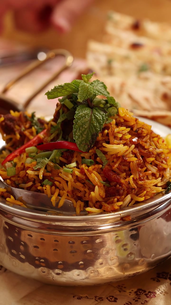 Panorámica de cámara en primer plano de auténtico arroz biryani indio, pan naan y raita de yogur cremosa.