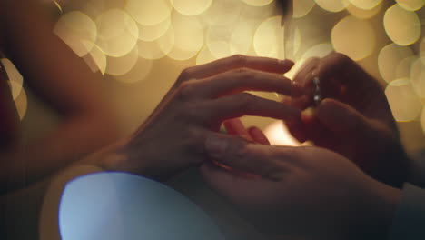 man hand wearing wedding ring at woman finger in evening blurred light closeup