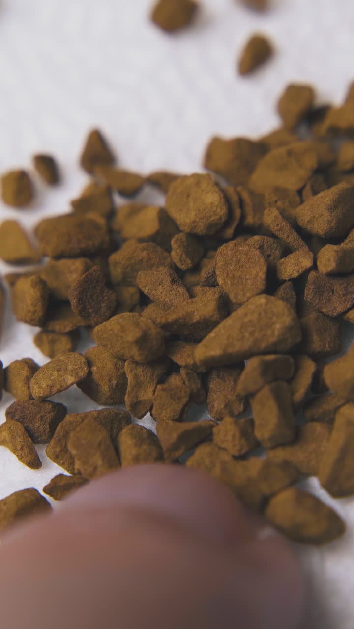 Junger Mann legt braunes trockenes Instantkaffeepulver aus der Handfläche auf eine weiße saubere Papierserviette, Makroaufnahme.