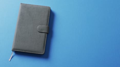 Close-up-of-closed-gray-notebook-with-copy-space-on-blue-background-in-slow-motion