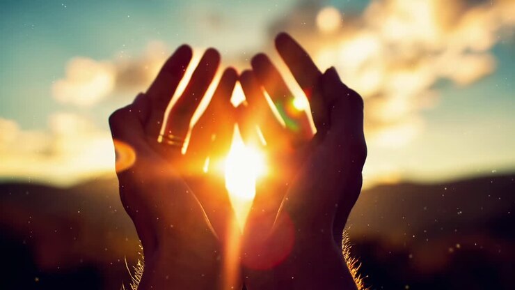 Hands framing the sun at sunset, captured from a low angle, creating a warm, cinematic video feel