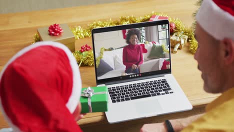 Padre-E-Hijo-Caucásicos-Con-Gorros-De-Papá-Noel-Usando-Una-Computadora-Portátil-Para-Una-Videollamada-Navideña-Con-Una-Mujer-En-La-Pantalla