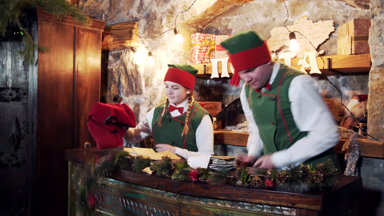 New Year preparation. Fairy elves taking out letters from sacks. Many envelopes from kids on the table in Santa's residence. Christmas atmosphere