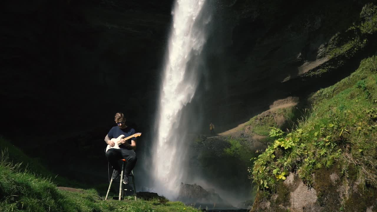 hombre tocando la guitarra frente a una hermosa cascada en islandia-20