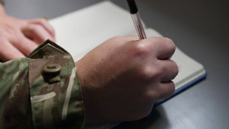 unrecognizable army soldier marine writing in a book or diary with a pen close up on hand