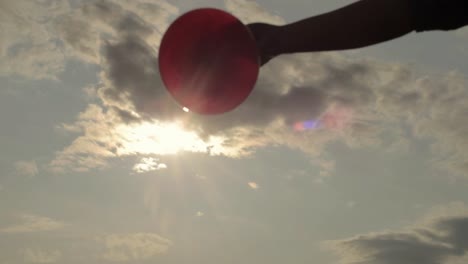 holding a red balloon against cloudscape