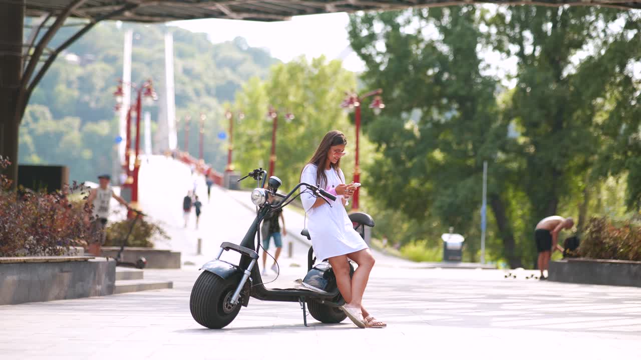 도시 공원에서 전기 스쿠터 에 스마트폰을 사용하는 여성