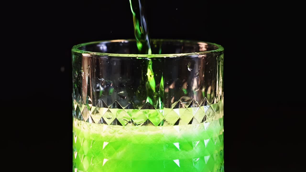 A vibrant green liquid is poured into a textured glass, creating a fizzy, bubbling effect.