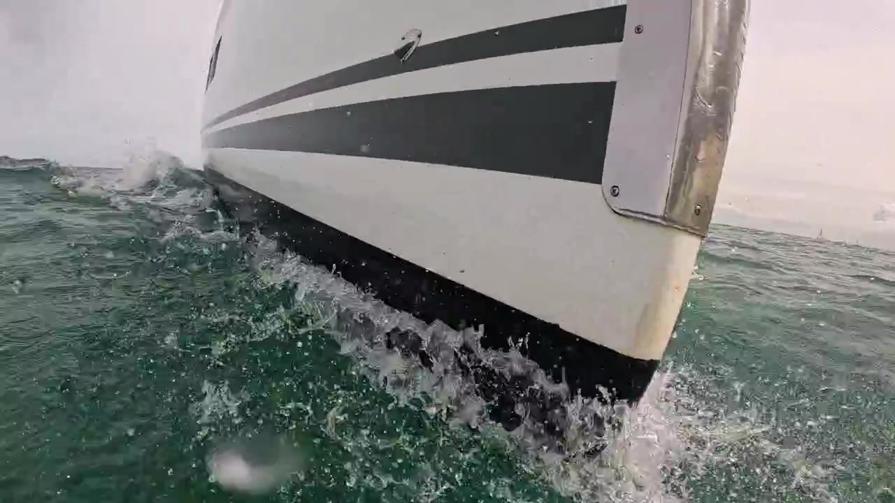 Scatto d'azione di una fotocamera semi-sommersa davanti a una barca a vela, che cattura spruzzi, onde di prua e il verde Mare del Nord dal livello dell'acqua. Gocce d'acqua che colpiscono l'obiettivo.