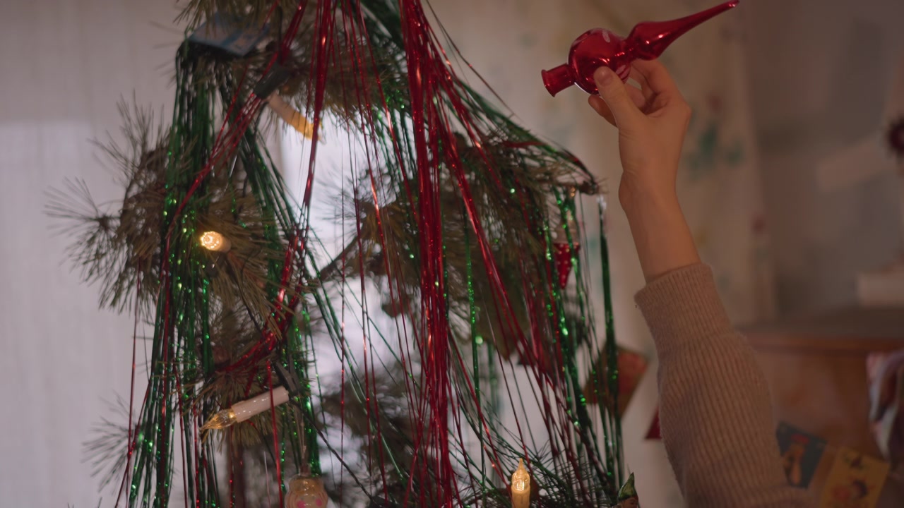 Colocação de decoração festiva. Arranjo cuidadoso de decorações de Natal coloridas em ambientes internos. Posicionamento meticuloso de decorações festivas brilhantes entre lâmpadas cintilantes e atmosfera alegre.