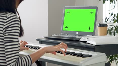 mujer joven tocando el piano electrónico aprendiendo remotamente usando una computadora portátil en casa. pantalla verde. llave de croma. concepto de educación y ocio en línea.