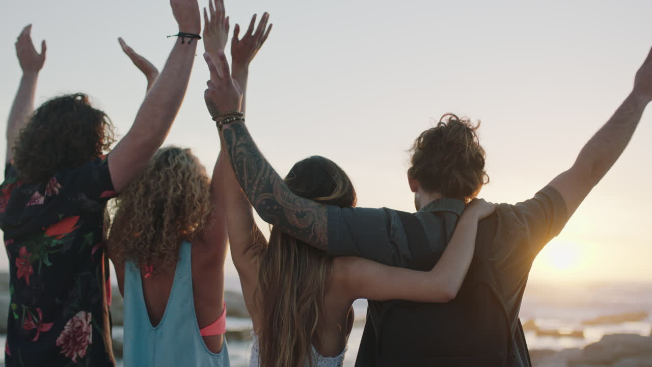 grupo de amigos abrazados en la playa celebrando con los brazos levantados al atardecer