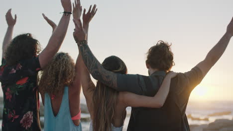 group of friends embracing on beach celebrating with arms raised at sunset