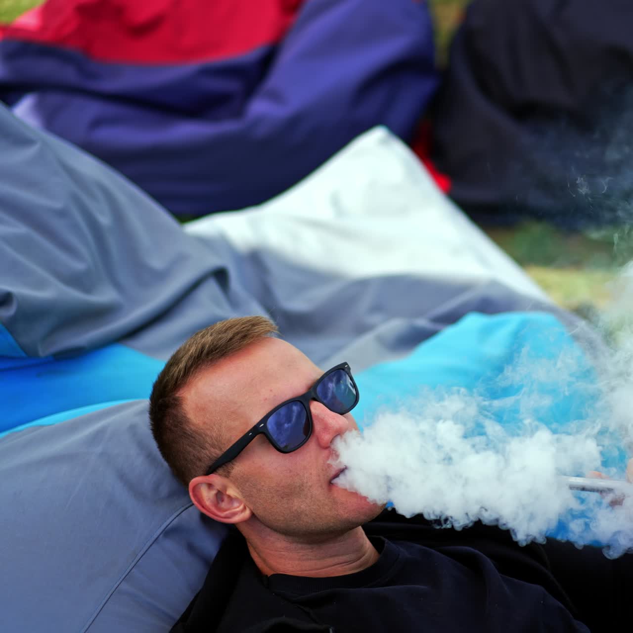 Male hookah smoker lies in bean bag chair outdoors. Man in sunglasses resting outside and looks at his laptop. View from above