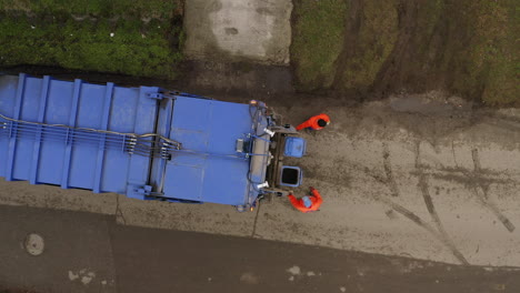 aerial top down descending shot of garbage truck collecting blue trash bins on cloudy day