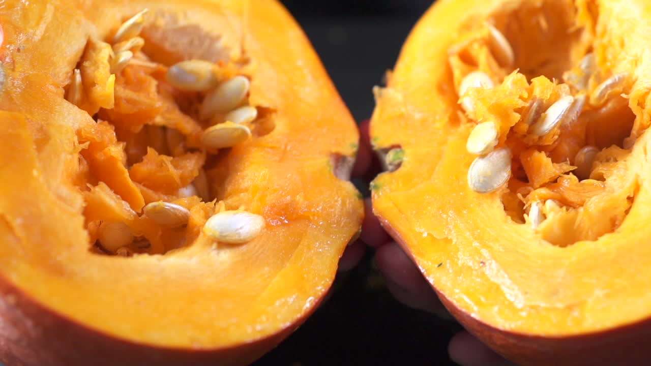 hands opening hokkaido pumpkin on slow motion on dark backdrop