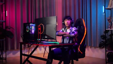 un adolescente asiático sonriendo a la cámara con los brazos cruzados mientras juega un videojuego en la computadora