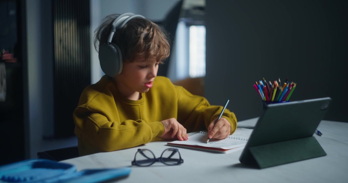 Young Boy in Headphones Writing and Studying with Tablet at Home