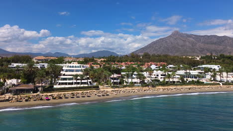 vista aérea de la playa de marbella y apartamentos con vistas a las montañas, casas de vacaciones de lujo en españa, destino de vacaciones de málaga, tiro de 4k moviéndose hacia adelante