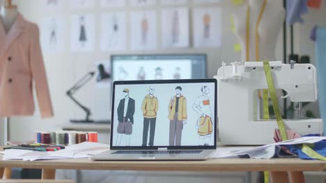 una computadora portátil está en la mesa mostrando imágenes de ropa en el estudio del diseñador