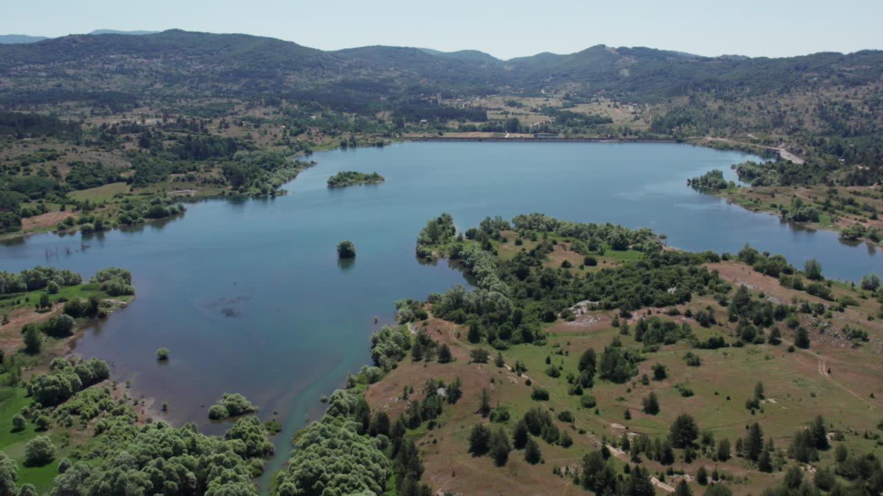 Ampia ripresa aerea con drone del lago di Tribistovo in Bosnia ed Erzegovina che mostra l'acqua blu, piccole isole, foreste e colline sotto la luce del sole estivo, per raccolte di filmati sulla natura, i viaggi e l'ambiente