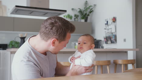 loving father holding 3 month old baby daughter in kitchen at home playing game