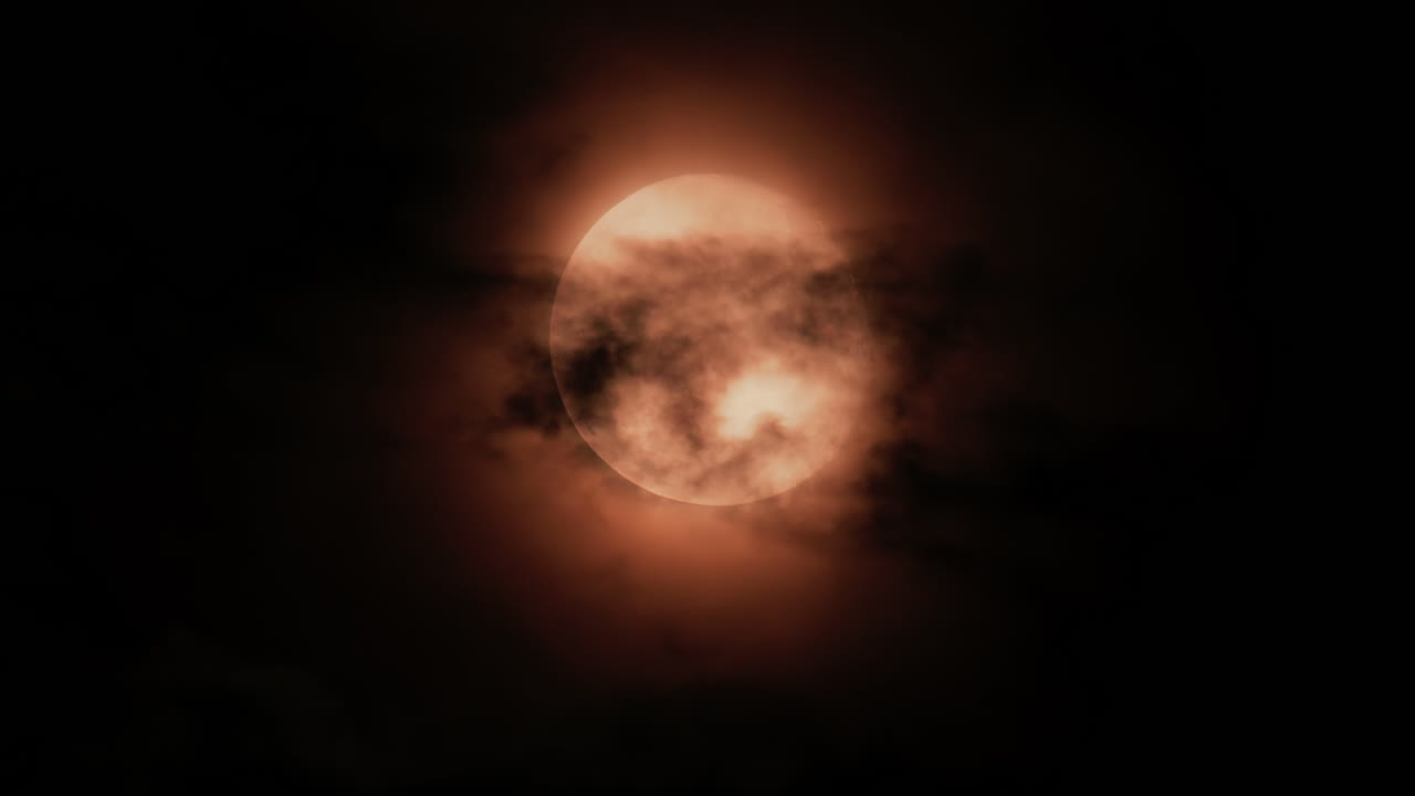 Close up of a full moon glowing through dark clouds at night