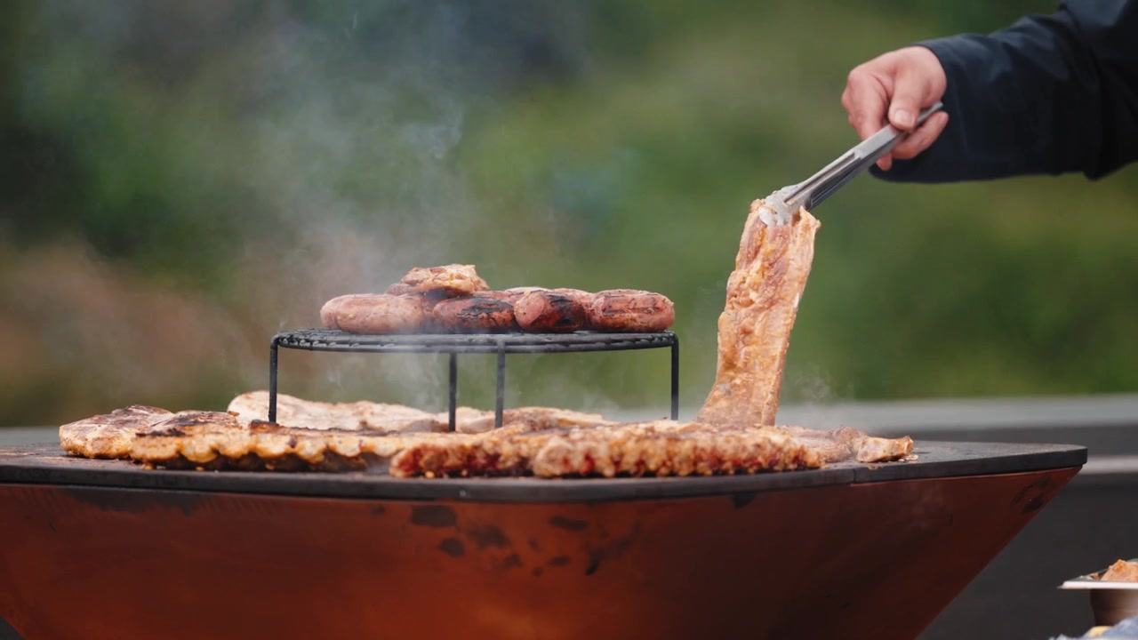 Le pinze sollevano un pezzo di maiale grigliato da una plancha d'acciaio fumante carica di carne.