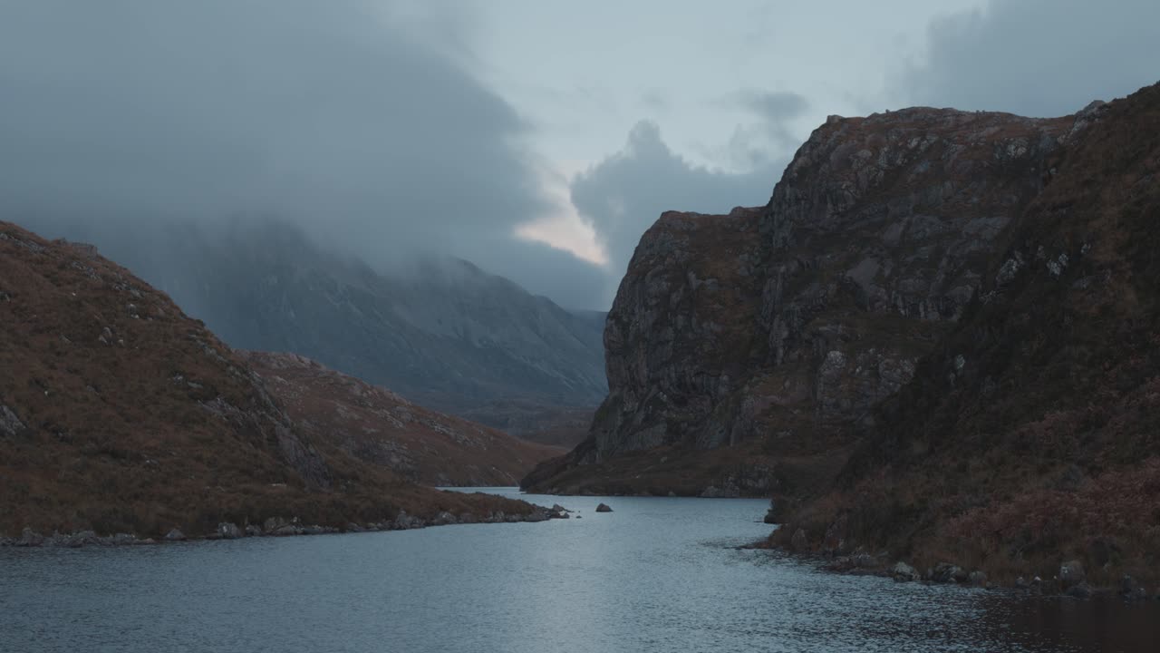 Slow upward tilt across a Scottish gorge, cool tones and drifting clouds wrapping the rugged cliffs, revealing tranquil highland atmosphere