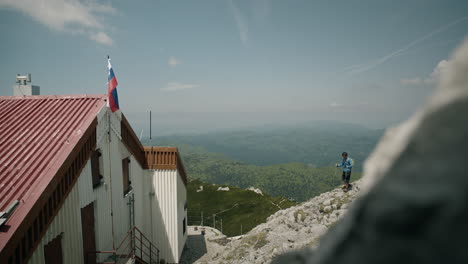 caminante caminando desde detrás de la roca hacia la cabaña en la montaña snežnik