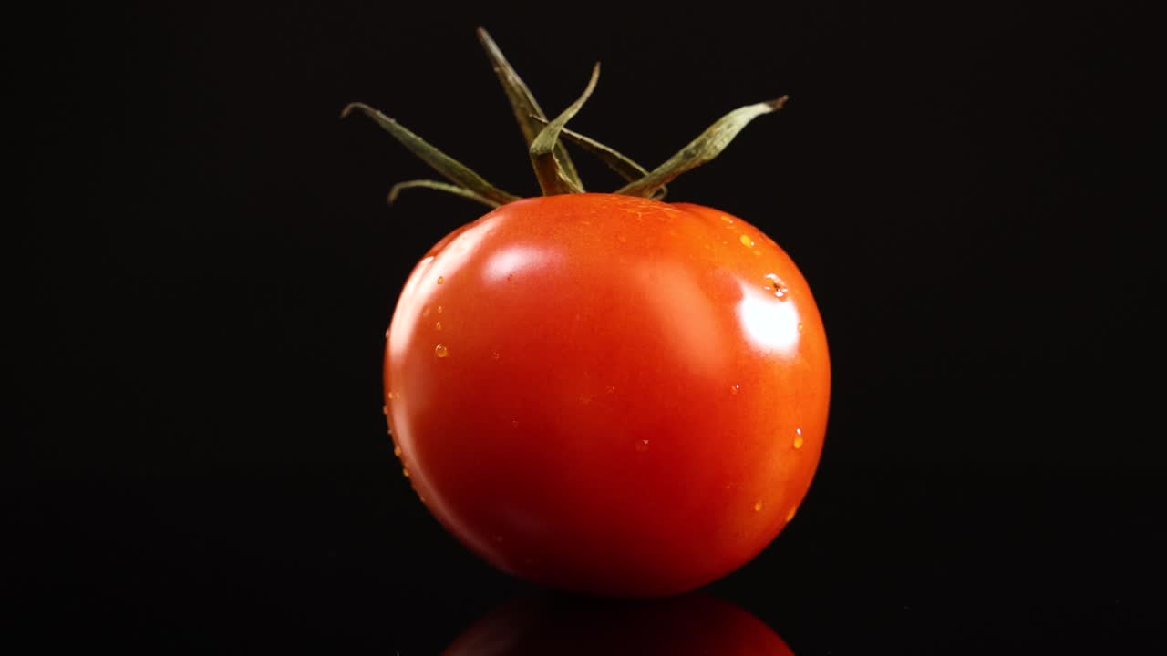 A ripe tomato rotates smoothly against a black background, illuminated by soft studio lighting. The camera remains steady, highlighting the tomato’s glossy texture and vibrant color